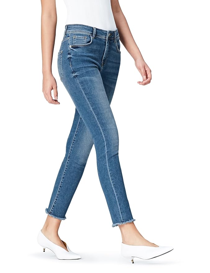 Vista lateral de unas piernas con jeans ajustados azules y tacones blancos sobre fondo claro